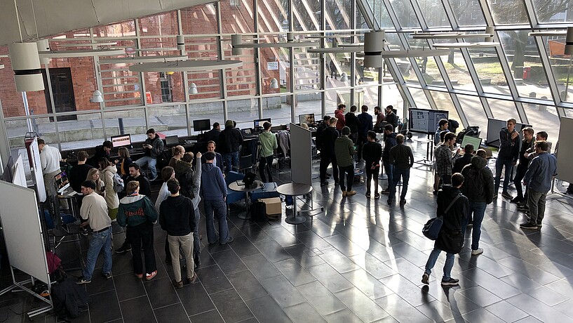 Das gläserne Foyer im Berliner Tor 5 mit vielen Studierenden die an Ständen in Gesprächen sind.