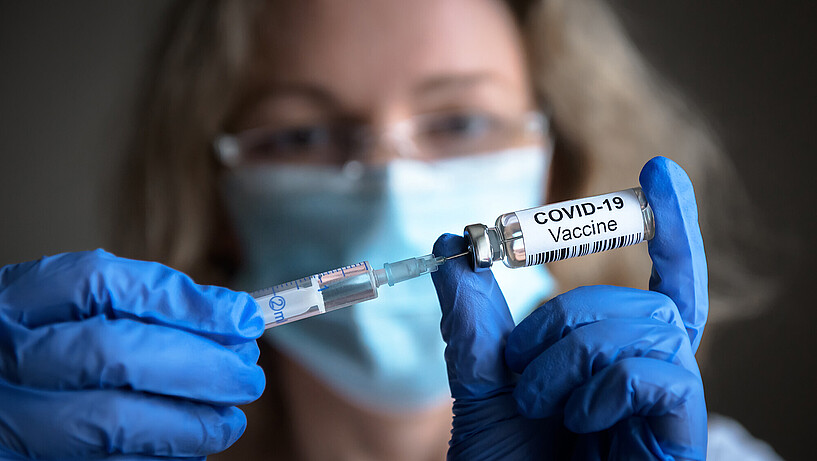Eine Frau zieht eine Spritze für eine Corona-Schutzimpfung auf.
